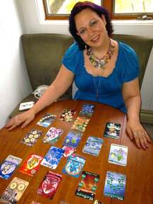 Zebrine, a woman wearing a blue dress, sits at a table with colorful cards